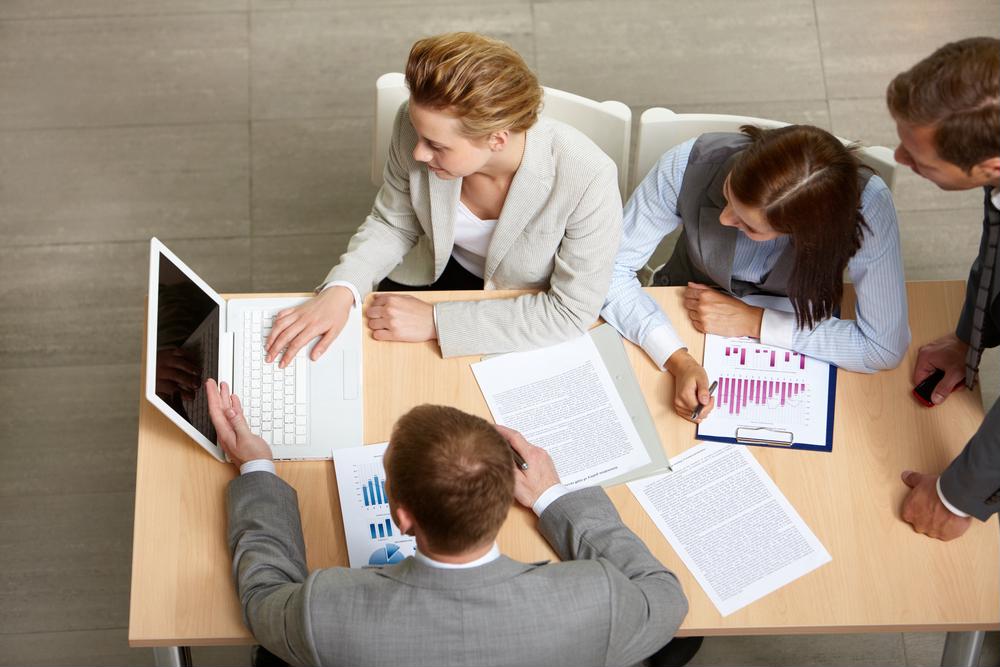 shot from above, looking at a group of people working at a table with a computer and papers displaying text and charts